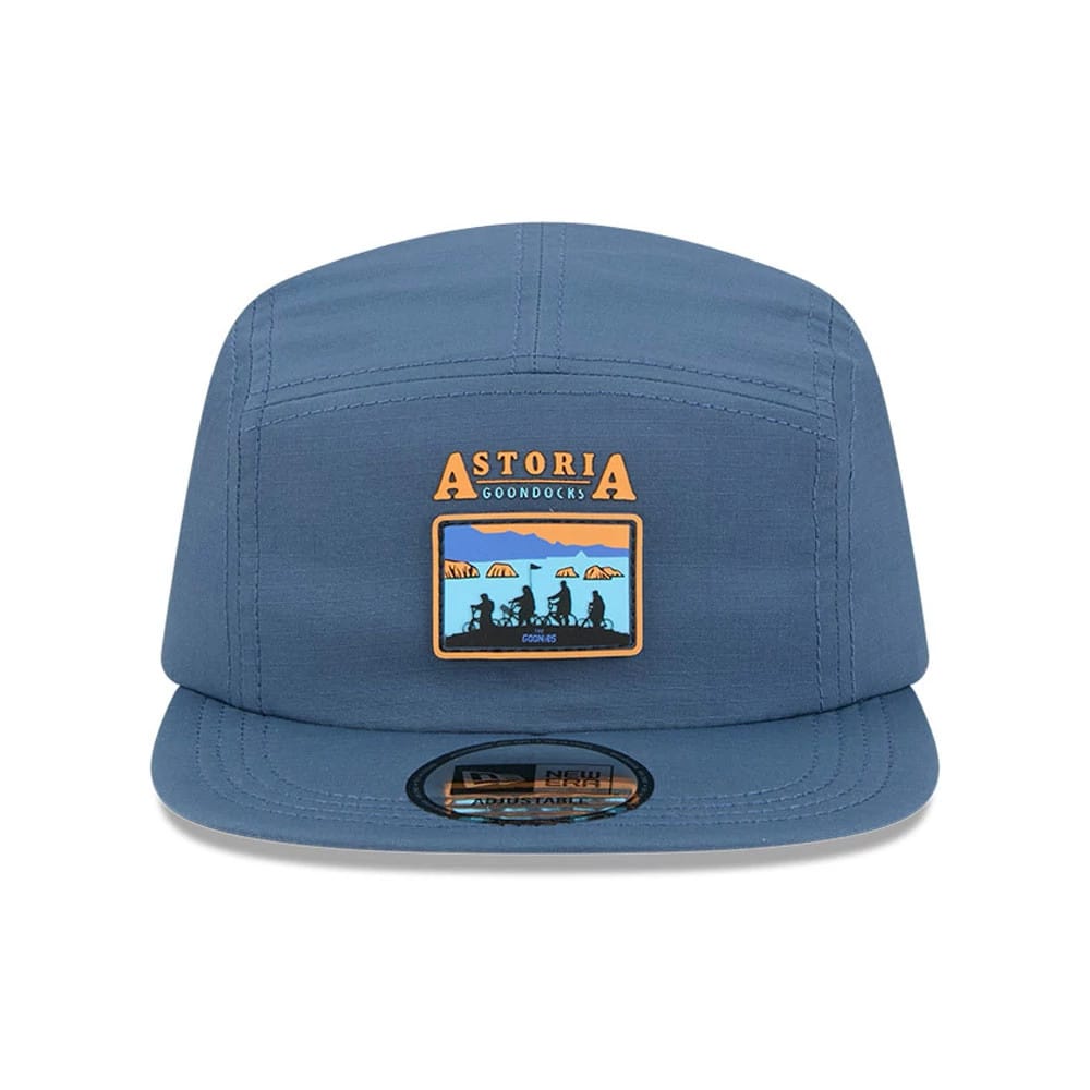 New Era The Goonies Astoria Warner Brothers Open Blue Camper Cap, front view showing a multi-colour embroidered patch with Astoria above silhouettes and a black adjustable size sticker on the blue visor.