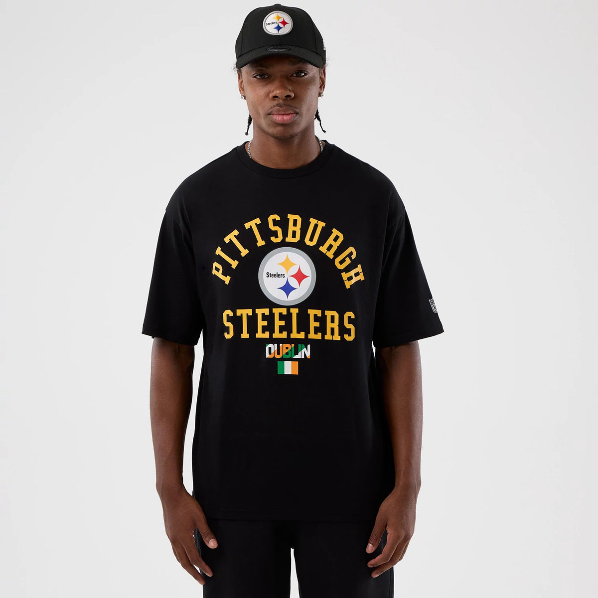 New Era Pittsburgh Steelers NFL International Series Games Black Oversized T-Shirt, front view on-model displaying the Pittsburgh Steelers lettering in yellow, a central team logo in white, and Dublin in green with the Irish flag below.