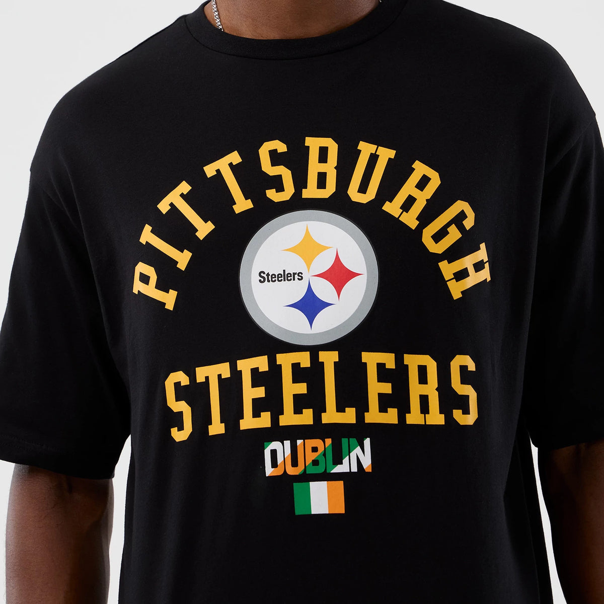 New Era Pittsburgh Steelers NFL International Series Games Black Oversized T-Shirt, front view showing the Pittsburgh Steelers logo printed at the centre, with yellow lettering above and below and a Dublin city name graphic with an Irish flag.