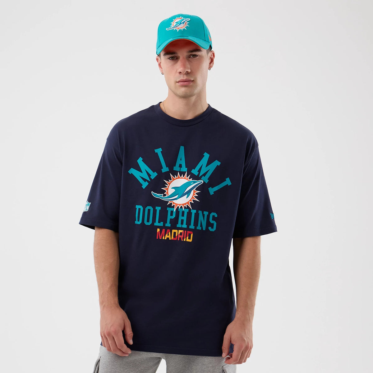 New Era Miami Dolphins NFL International Series Games Navy Oversized T-Shirt, front view on-model showing turquoise Miami Dolphins lettering across the chest, with the team logo in the centre above red Madrid text.