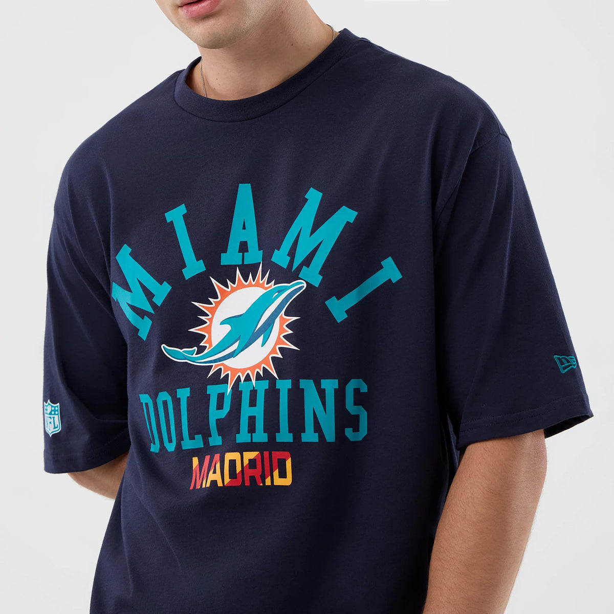 New Era Miami Dolphins NFL International Series Games Navy Oversized T-Shirt, front view on-model displaying the Miami Dolphins logo and MADRID lettering in colours across the chest, with an embroidered New Era flag logo on the sleeve.