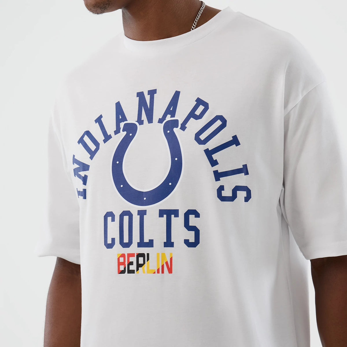 New Era Indianapolis Colts NFL International Series Games White Oversized T-Shirt, front view showing blue printed Indianapolis Colts lettering and horseshoe design, with Berlin lettering in red and yellow beneath