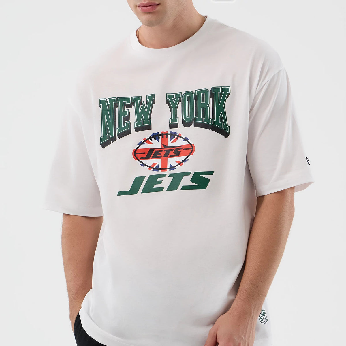 New Era New York Jets NFL International Series Games White Oversized T-Shirt, front view on-model featuring large green New York Jets lettering and a Union Jack football graphic printed across the chest, with a small printed logo on the sleeve.