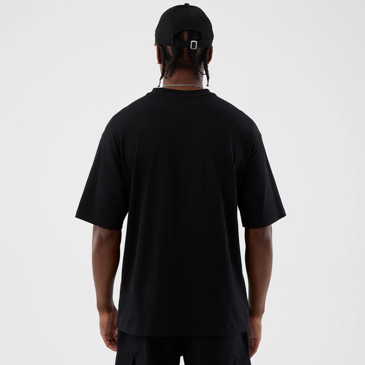 New Era Berlin NFL International Series Games Black Oversized T-Shirt, back view on a model paired with a black cap, showing the plain black rear with a relaxed fit extending below the waist.