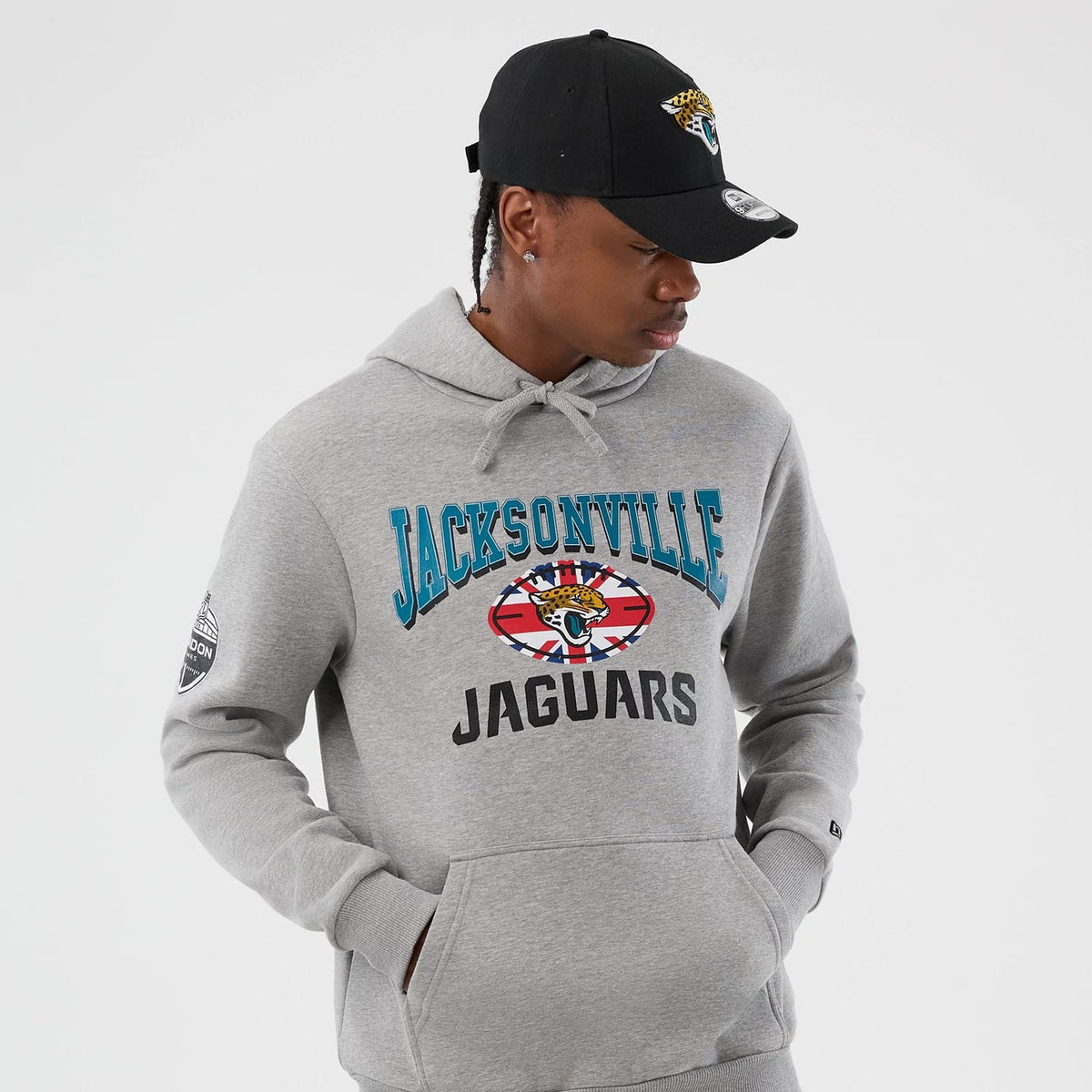 New Era Jacksonville Jaguars NFL International Series Games Grey Pullover Hoodie, front view on-model showing turquoise Jacksonville lettering above a jaguar logo with UK flag elements, Jaguars in black below.