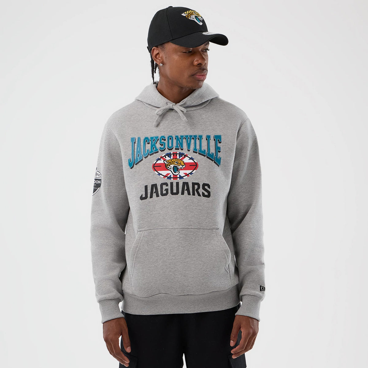 New Era Jacksonville Jaguars NFL International Series Games Grey Pullover Hoodie, front view on a model wearing a black cap, showcasing teal and black team graphics on the chest and an embroidered New Era logo on the cuff.