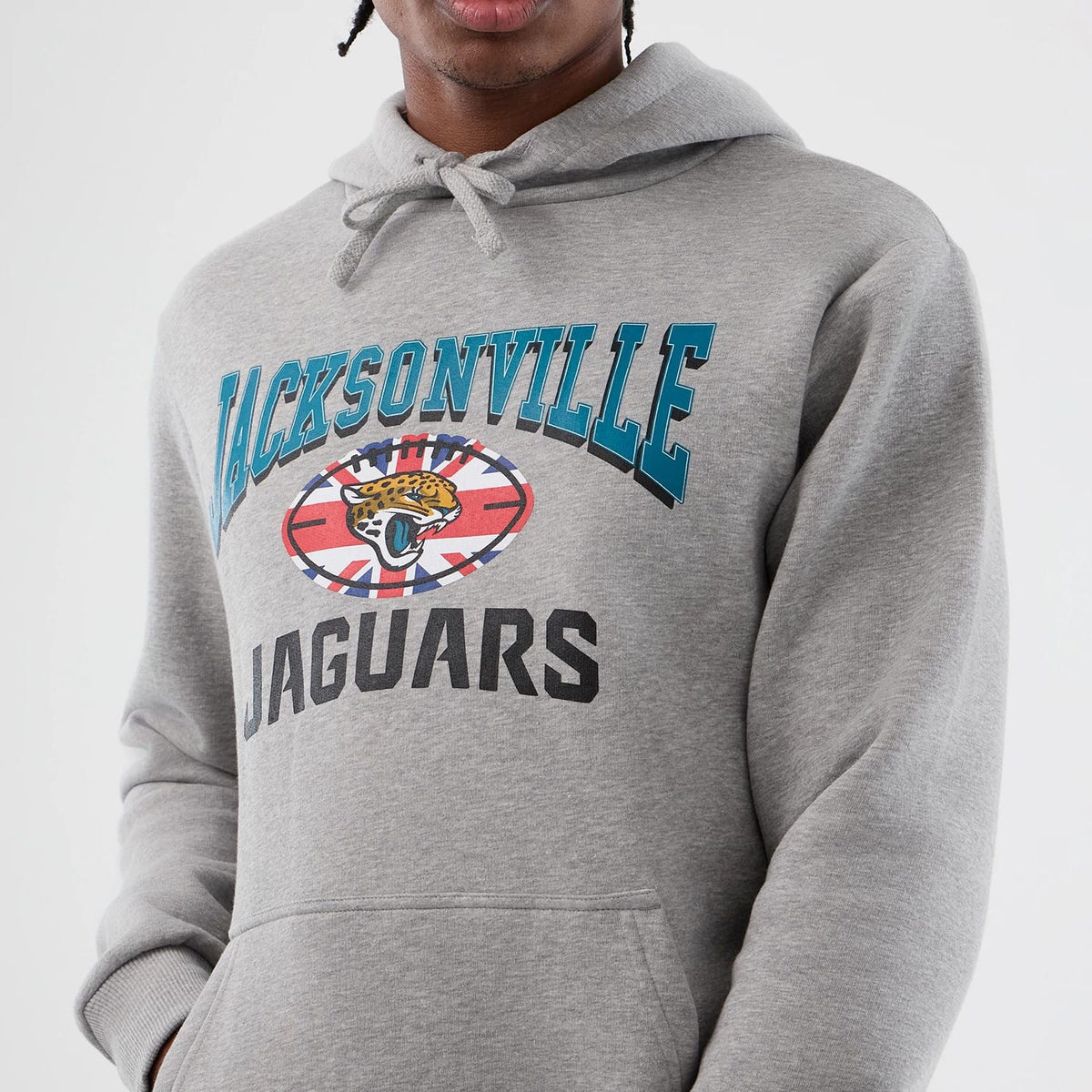 New Era Jacksonville Jaguars NFL International Series Games Grey Pullover Hoodie, front view on a model showing the Jaguars emblem at the centre, Jacksonville lettering arched above in teal and Jaguars text below in black on the grey fabric.