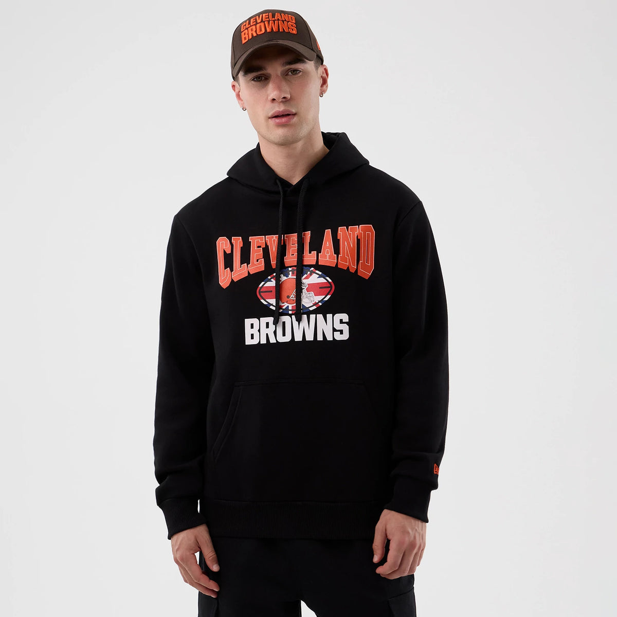 New Era Cleveland Browns NFL International Series Games Black Pullover Hoodie, front view on-model showing orange Cleveland lettering above a central team logo and white Browns text, worn with a matching cap.