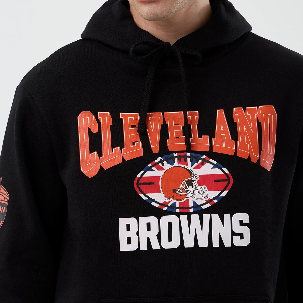 New Era Cleveland Browns NFL International Series Games Black Pullover Hoodie, front view showing printed Cleveland Browns graphics with an American football helmet over a Union Jack design on the chest and additional printed emblem on the sleeve.