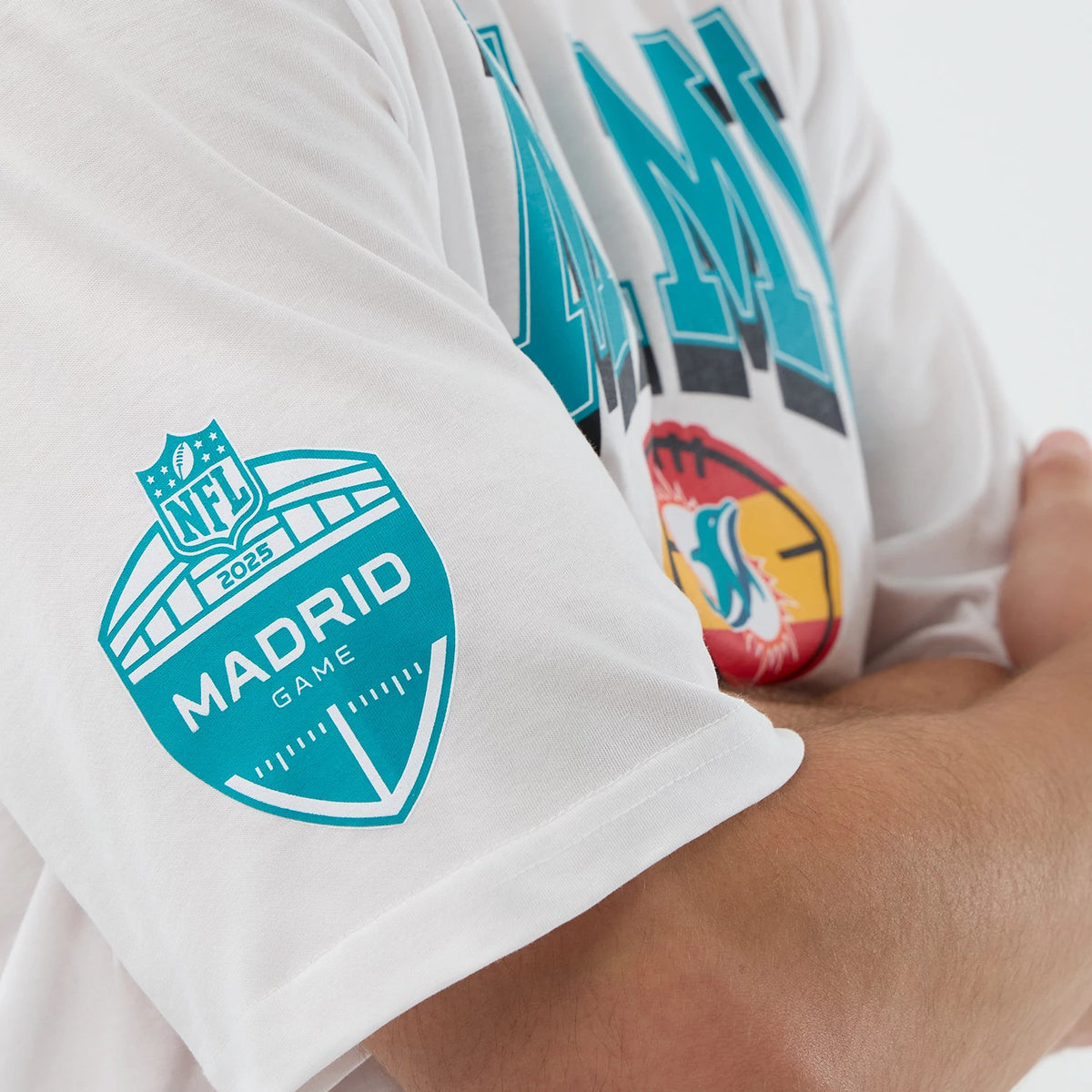 New Era Dolphins NFL International Series Games Madrid White Oversized T-Shirt, side view on a model showing the blue printed NFL 2025 Madrid Game logo on the sleeve and a colourful Dolphins football graphic on the chest.