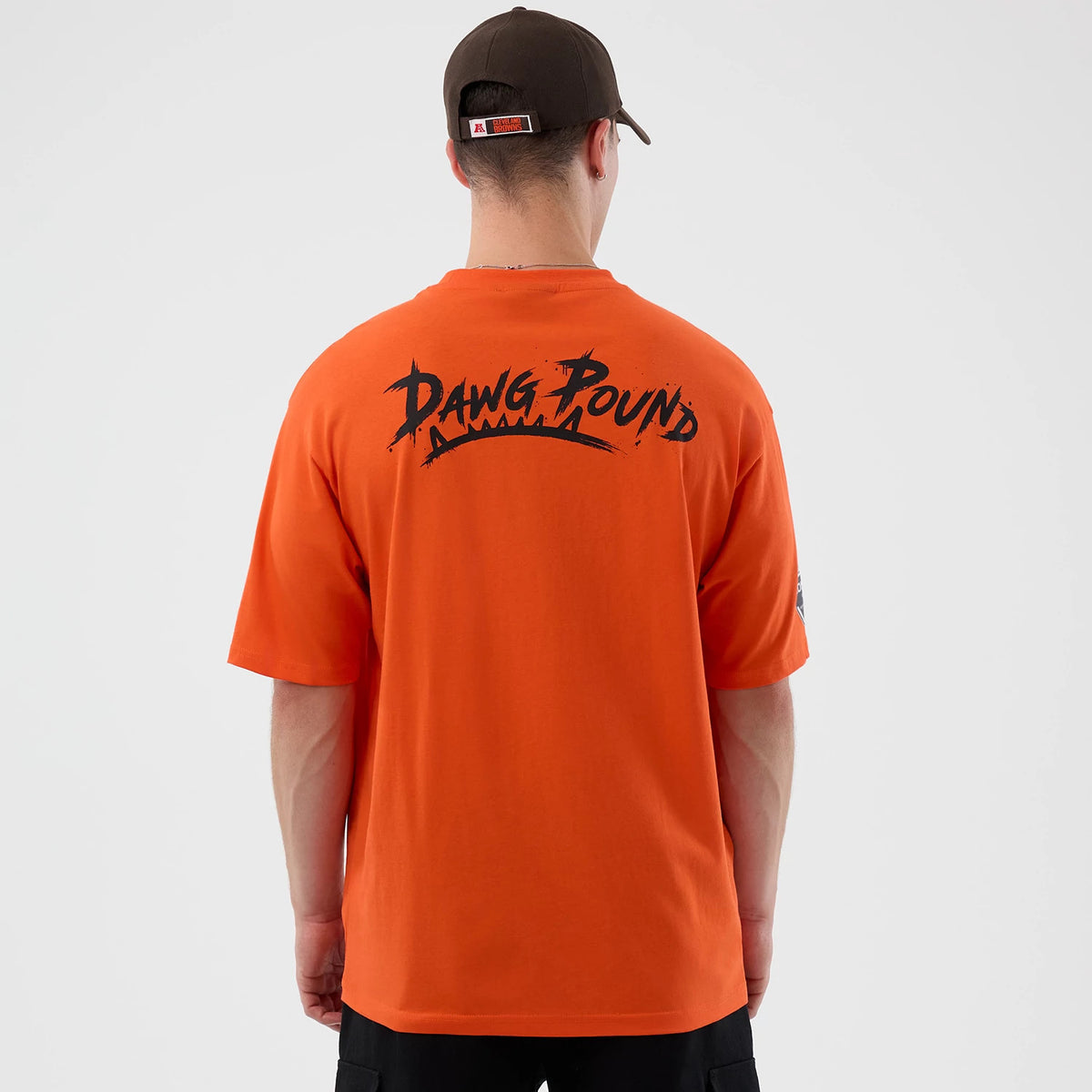 New Era Cleveland Browns NFL International Series Games Orange Oversized T-Shirt, back view on a model showing black Dawg Pound lettering across the upper back with sleeves extending just above the elbows.