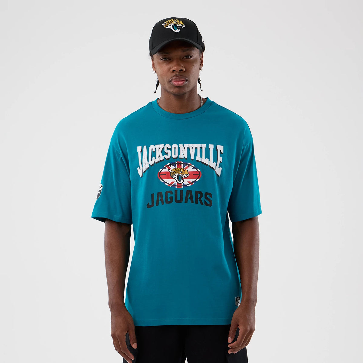 New Era Jacksonville Jaguars NFL International Series Games Turquoise Oversized T-Shirt, front view on-model featuring white Jacksonville lettering above a large printed team logo and Jaguars lettering, with an additional patch on the sleeve.
