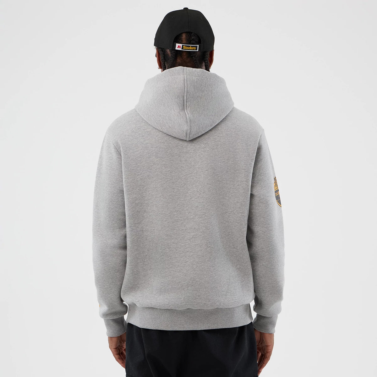 New Era Pittsburgh Steelers NFL International Series Games Grey Pullover Hoodie, back view on a model wearing a black cap, showing the plain grey back with a large hood and an embroidered Steelers logo on the left sleeve.