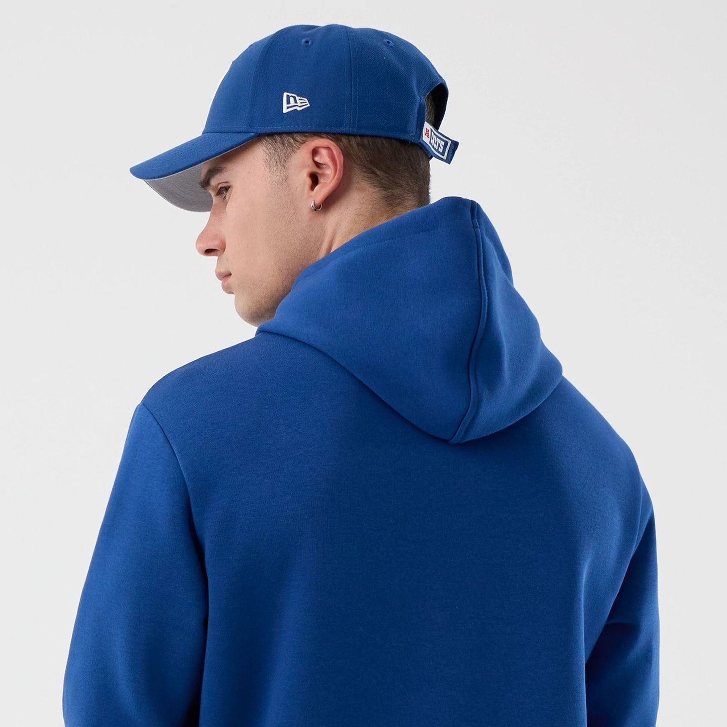 New Era Indianapolis Colts NFL International Series Games Blue Pullover Hoodie, back view on-model showing the rich blue hood and plain back, paired with a blue cap featuring an embroidered New Era logo on the side.