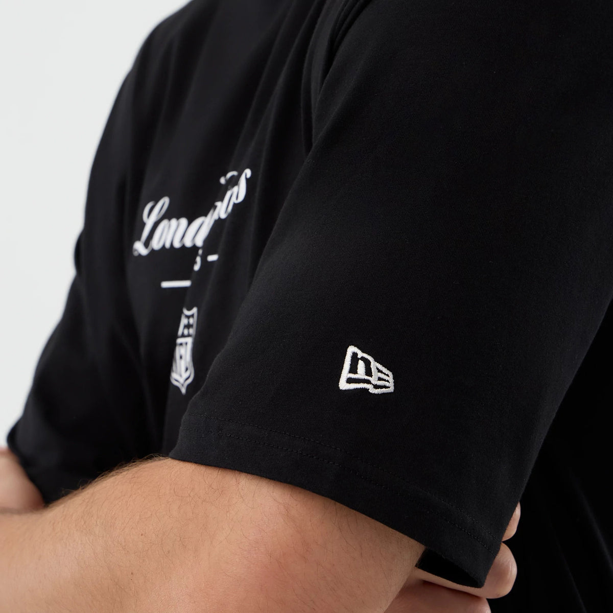 New Era London Games NFL International Series Games Black Oversized T-Shirt, three-quarter view focusing on the short sleeve with the embroidered New Era logo in white, and a glimpse of the London Games lettering on the chest.