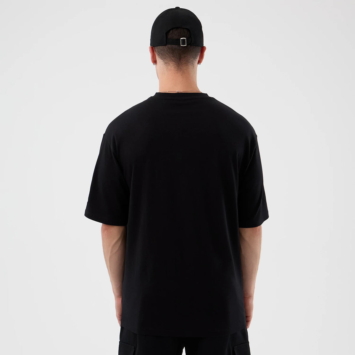 New Era London Games NFL International Series Games Black Oversized T-Shirt, back view on a model, showcasing the simple black design without graphics or lettering, paired with a black cap, highlighting the minimalistic style.