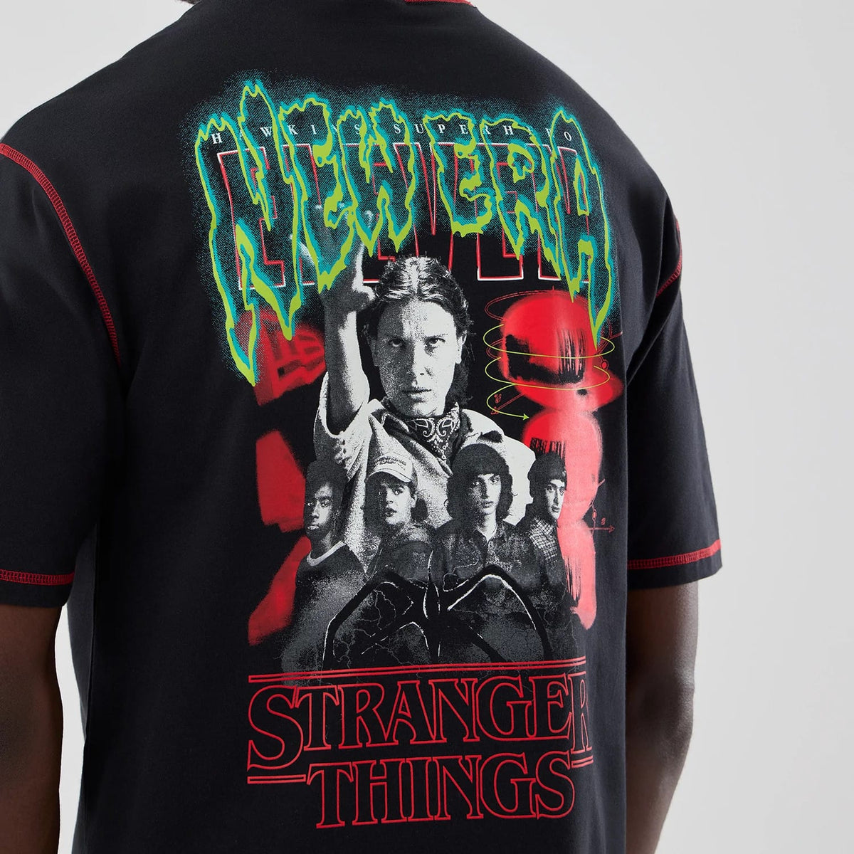 New Era Stranger Things Black Oversized T-Shirt, back view showing a graphic with characters from the series, green and red New Era lettering above, and Stranger Things text below, worn by a model.