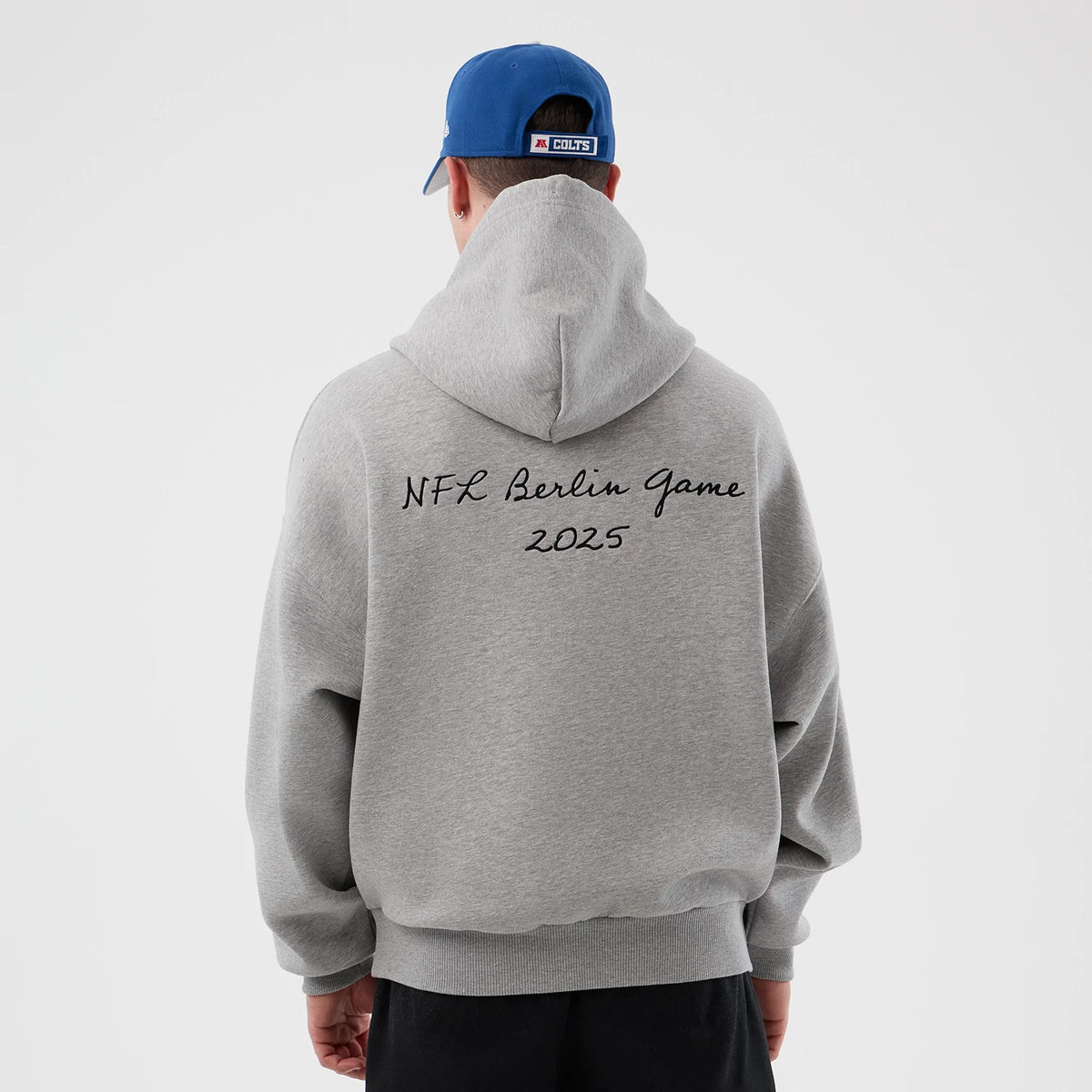 New Era Indianapolis Colts NFL International Series Games Grey Pullover Hoodie, back view on a model with a blue cap, displaying NFL Berlin Game 2025 in black lettering across the upper back, complete with a relaxed hood.