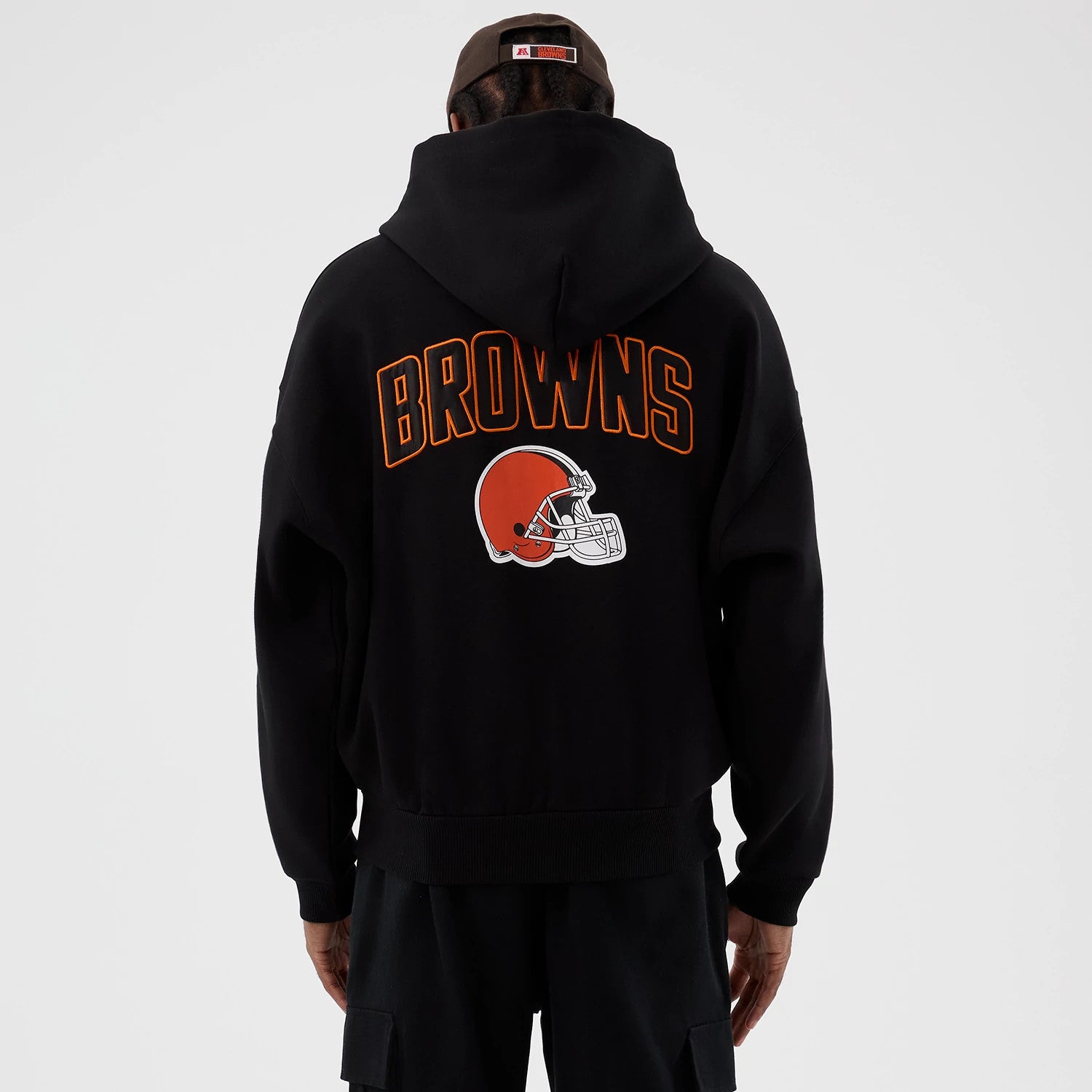 New Era Cleveland Browns NFL International Series Games Black Full Zip Hoodie, back view on a model showing Browns lettering and the orange helmet logo printed on the hoodie’s back in contrasting colours, with the hood up.