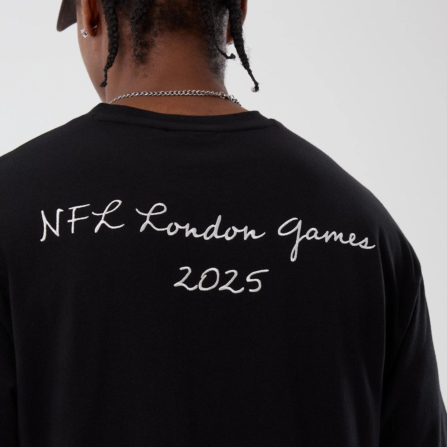 New Era Cleveland Browns NFL International Series Games Black Oversized T-Shirt, back view showing white embroidered text NFL London Games 2025 across the upper back on a plain black background, styled with a cap on a model.