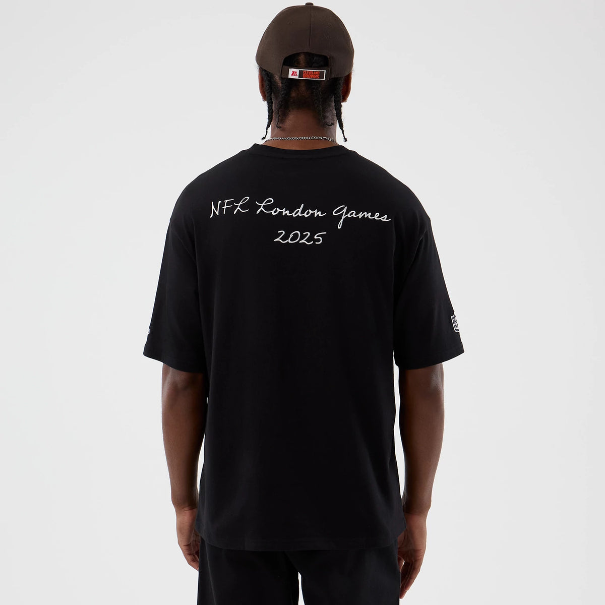 New Era Cleveland Browns NFL International Series Games Black Oversized T-Shirt, back view on a model with a cap, showing NFL London Games 2025 lettering across the upper back and embroidered logos on the sleeves.