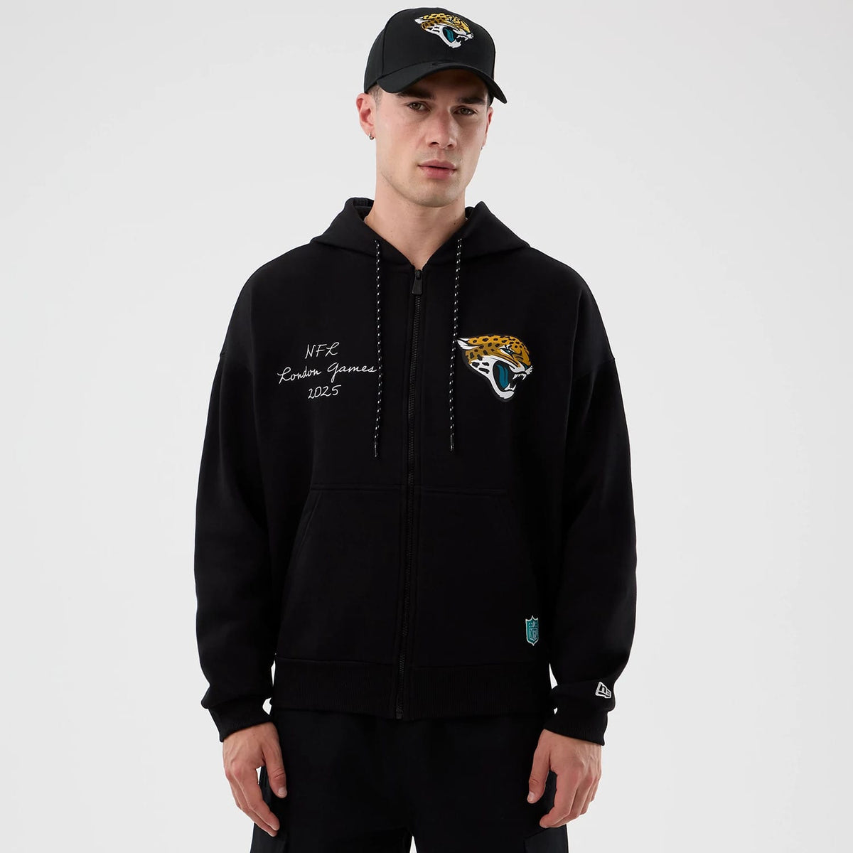 New Era Jacksonville Jaguars NFL International Series Games Black Full Zip Hoodie, front view on-model showing the embroidered Jaguars logo on the chest, NFL London Games 2025 lettering on the shoulder, and raised New Era flag logo on the sleeve.