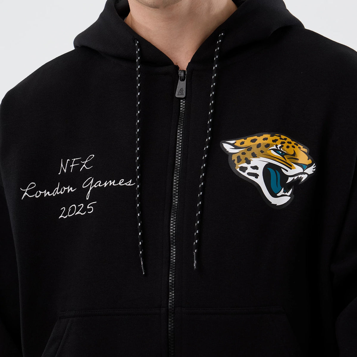 New Era Jacksonville Jaguars NFL International Series Games Black Full Zip Hoodie, front view showing the embroidered 'NFL London Games 2025' script on the left and the printed jaguar logo on the right of the chest, with a central zip.