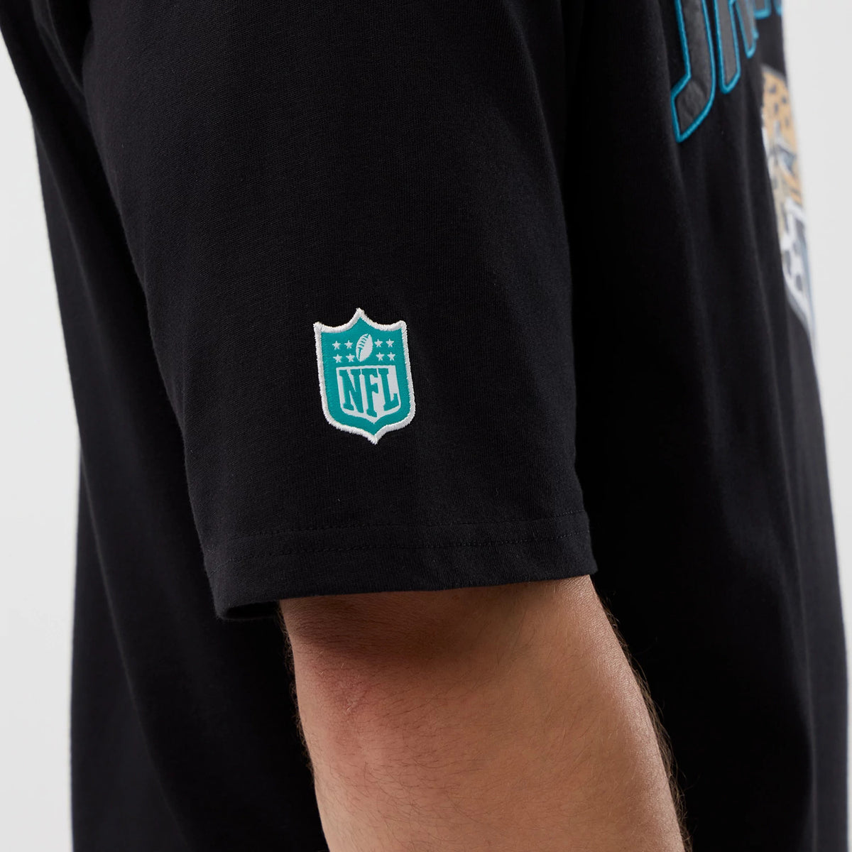 New Era Jaguars NFL International Series Games Script Black Oversized T-Shirt, side view showing the white embroidered NFL logo on the sleeve with the Jaguars script partially in blue on a black background.