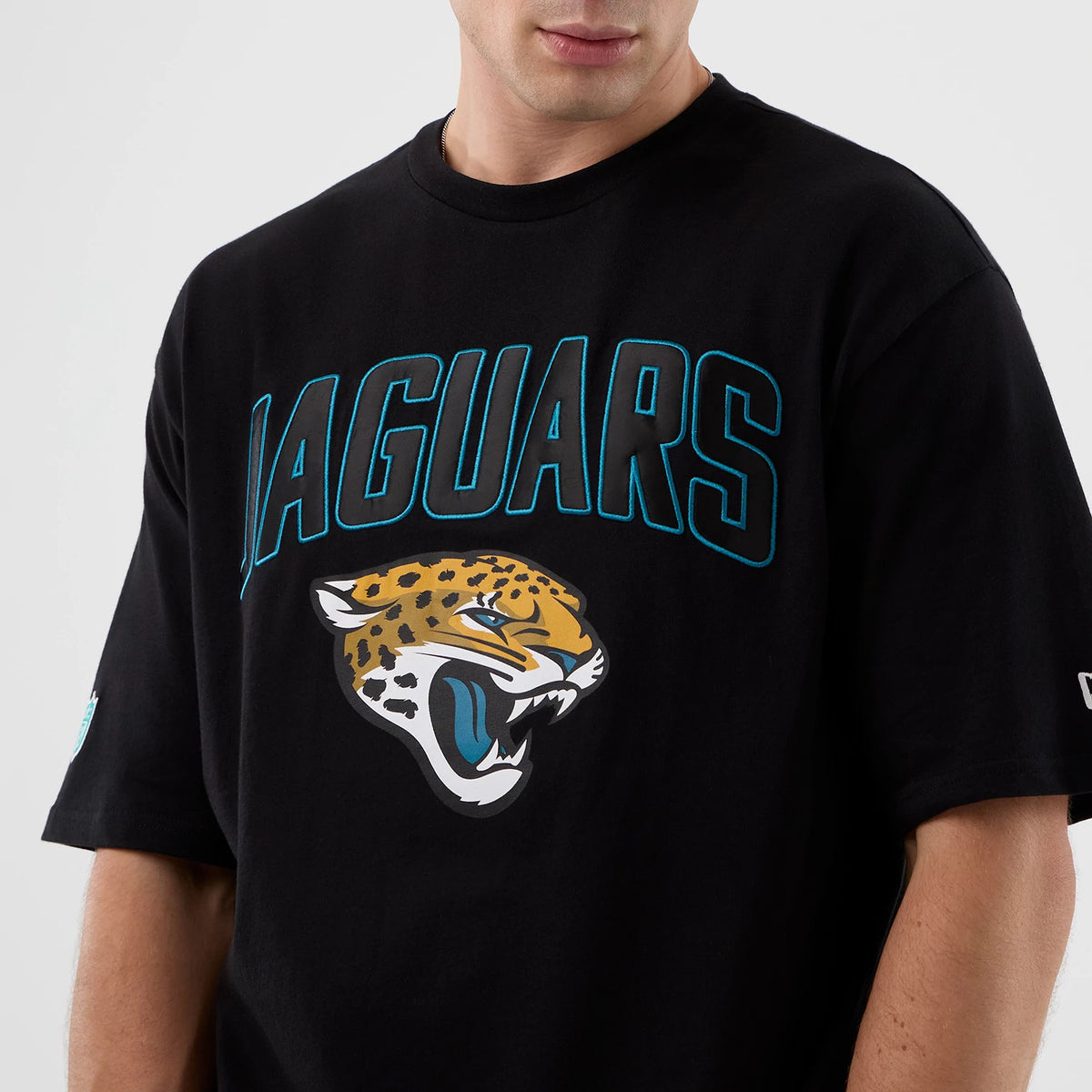 New Era Jaguars NFL International Series Games Script Black Oversized T-Shirt, front view on-model showing the JAGUARS lettering in blue above a fierce embroidered jaguar head logo, with a New Era logo on the sleeve.