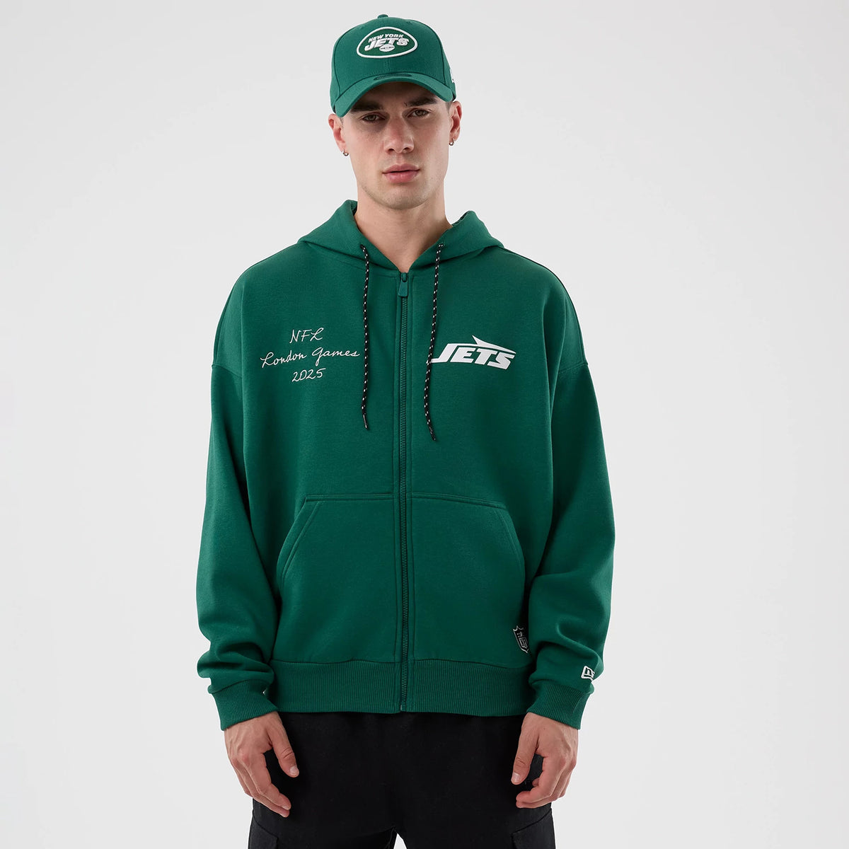 New Era New York Jets NFL International Series Games Green Full Zip Hoodie, front view on-model showing white embroidered Jets logo on the chest, NFC London Games 2023 lettering on the left, and drawstring hood, paired with a matching cap.