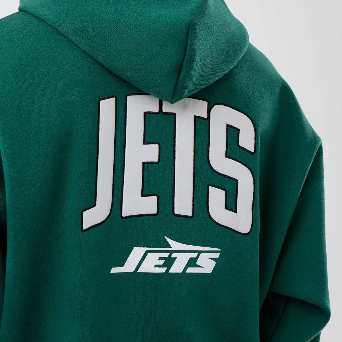 New Era New York Jets NFL International Series Games Green Full Zip Hoodie, back view showing large white JETS lettering across the upper back and a white Jets logo underneath against the rich green fabric, with the hood at the top.