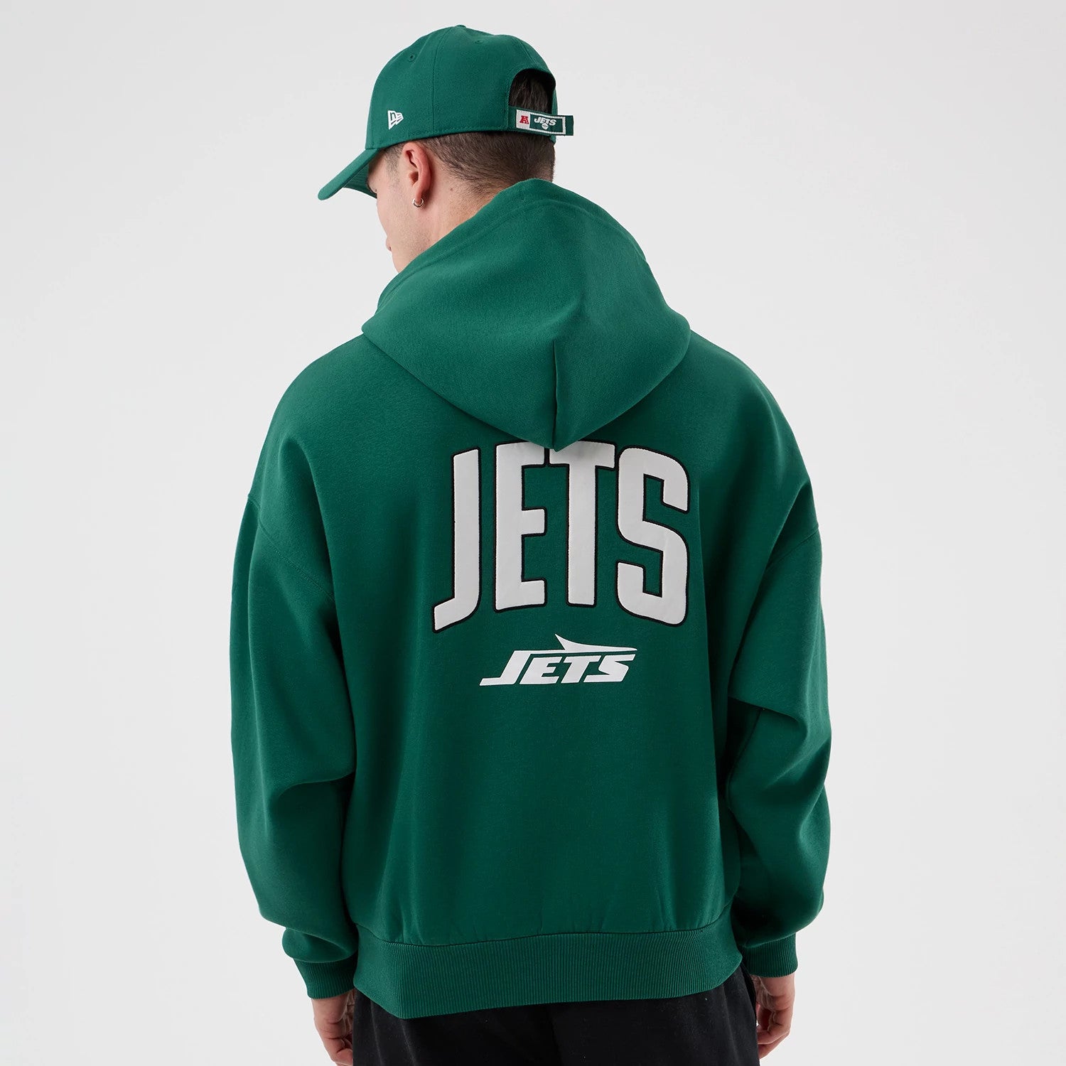 New Era New York Jets NFL International Series Games Green Full Zip Hoodie, back view on a model also wearing a cap, featuring large white JETS lettering across the upper back and a smaller Jets logo underneath on the green hoodie.