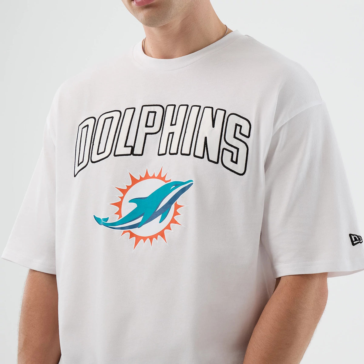 New Era Dolphins NFL International Series Games Script White Oversized T-Shirt, front view showing the Dolphins lettering and teal dolphin logo, with an embroidered New Era logo on the left sleeve on a white backdrop.
