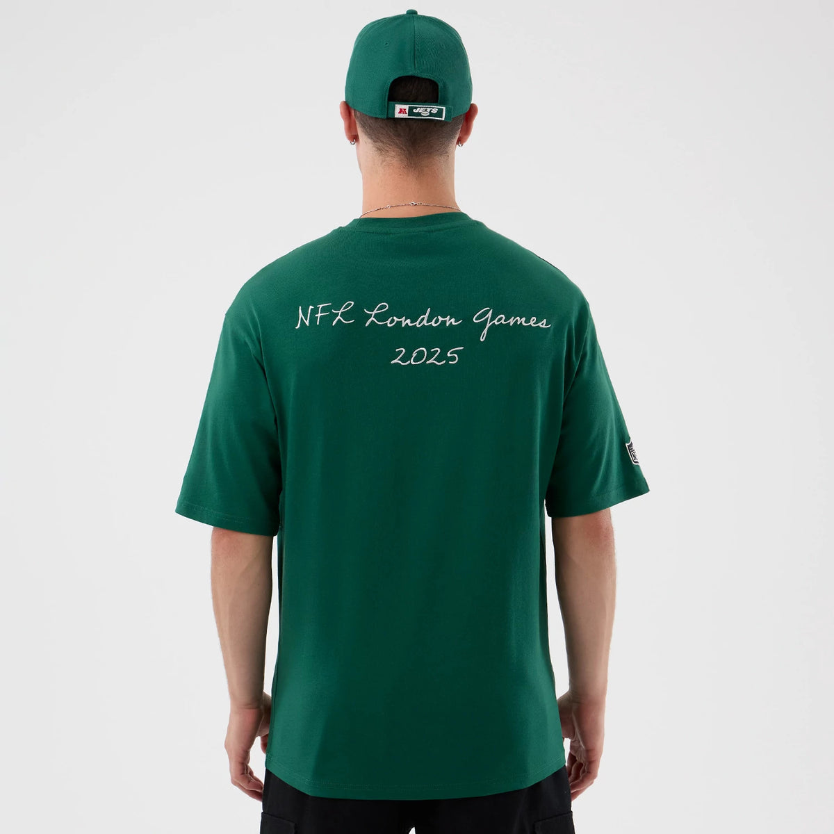New Era New York Jets NFL International Series Games Green Oversized T-Shirt, back view on a model featuring NFL London Games 2025 lettering in white script across the upper back, paired with a matching green cap.