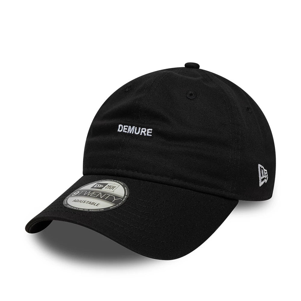 New Era Slogan Demure Black 9TWENTY Adjustable Cap, front view with white Demure embroidery on the unstructured black crown, a curved visor with a 9TWENTY size sticker, and New Era flag logo on the left side.