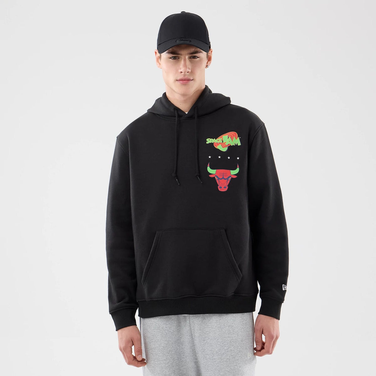New Era Chicago Bulls Space Jam 2 X NBA Black Pullover Hoodie, front view on-model showing the colourful Space Jam and Bulls logo printed on the chest, with a kangaroo pocket below and an embroidered New Era logo on the sleeve.