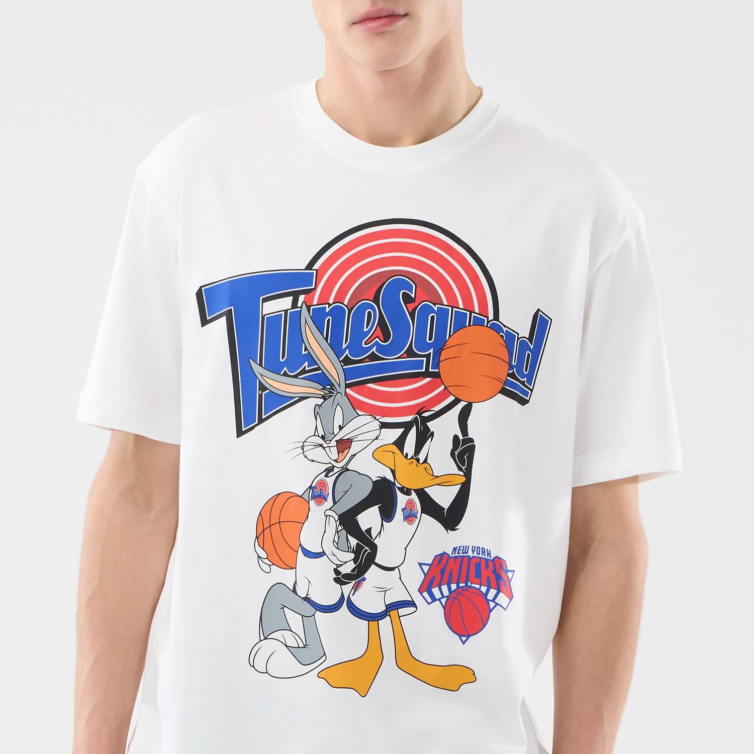New Era New York Knicks Space Jam 2 X NBA White T-Shirt, front view on-model showing a large colourful graphic of Bugs Bunny and Daffy Duck holding basketballs with Tune Squad above, and the New York Knicks logo at the bottom.