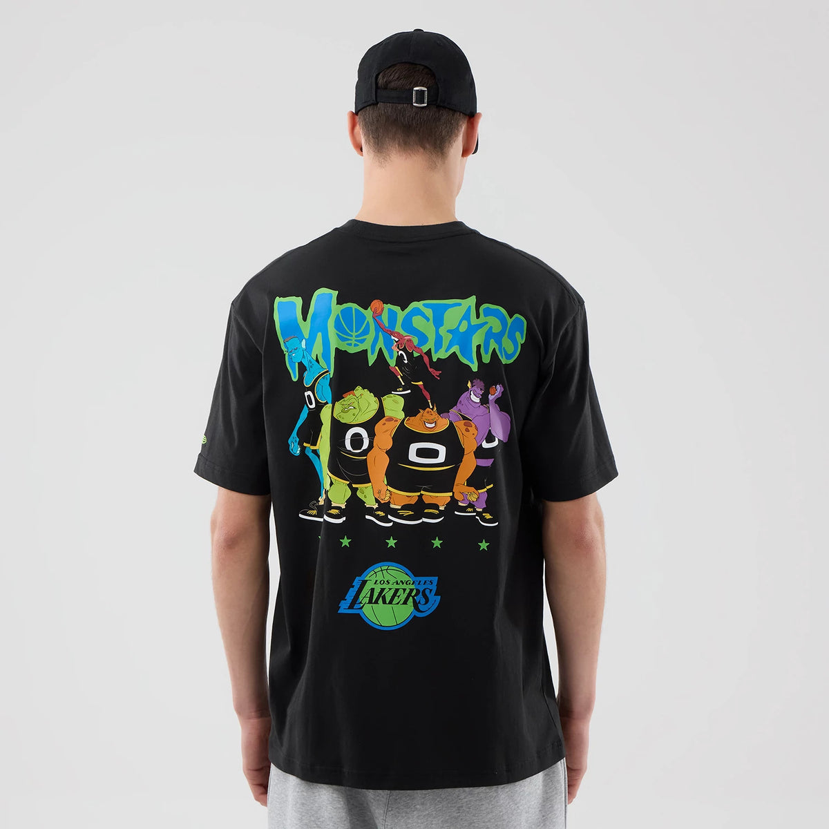 New Era LA Lakers Space Jam 2 X NBA Black T-Shirt, back view on a model with a black cap showing a colourful graphic of Monstars characters and lettering, with the Los Angeles Lakers logo printed near the bottom.