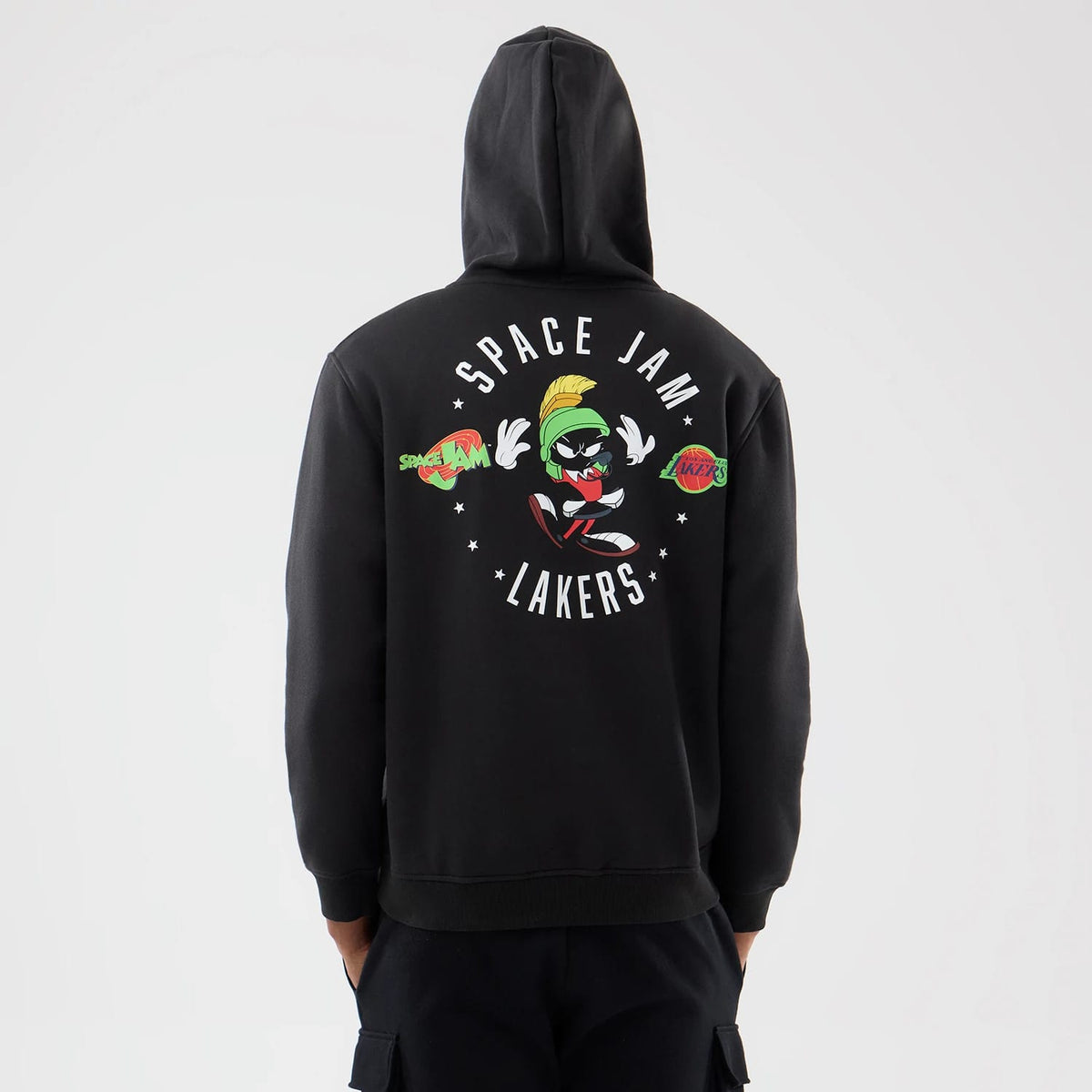 New Era LA Lakers Space Jam 2 X NBA Black Pullover Hoodie, back view showing printed Space Jam graphics with Marvin the Martian at the centre, surrounded by Space Jam and Lakers logos, worn with dark trousers.