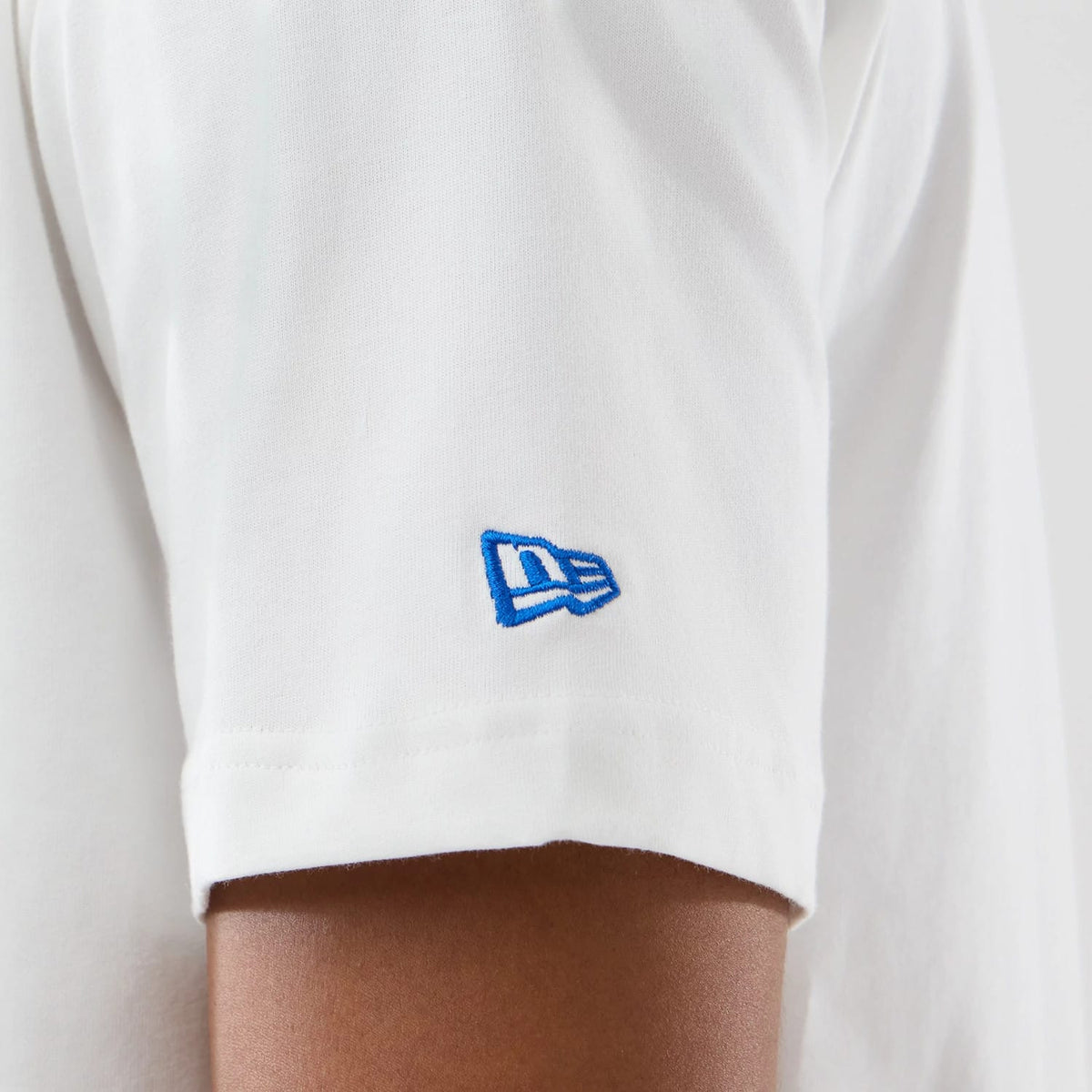 New Era LA Lakers Space Jam 2 X NBA White T-Shirt, side view showing a close-up of the sleeve with a blue embroidered New Era flag logo positioned near the hem on the plain white fabric.