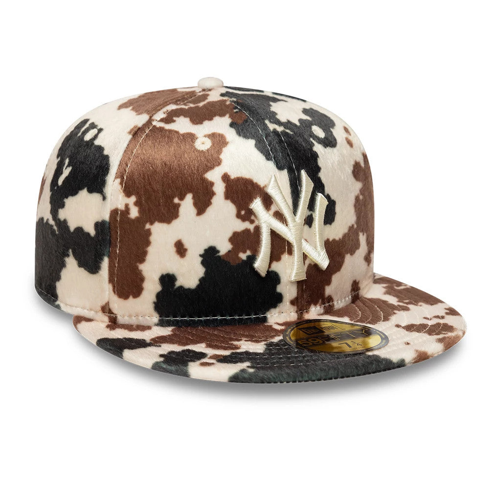 New York Yankees Animal Print Cow Beige New Era 59FIFTY Fitted Cap, three-quarter view showing the beige embroidered NY logo on the front panel, a cow print pattern in brown, black, and beige, and a gold 59FIFTY size sticker on the flat visor.