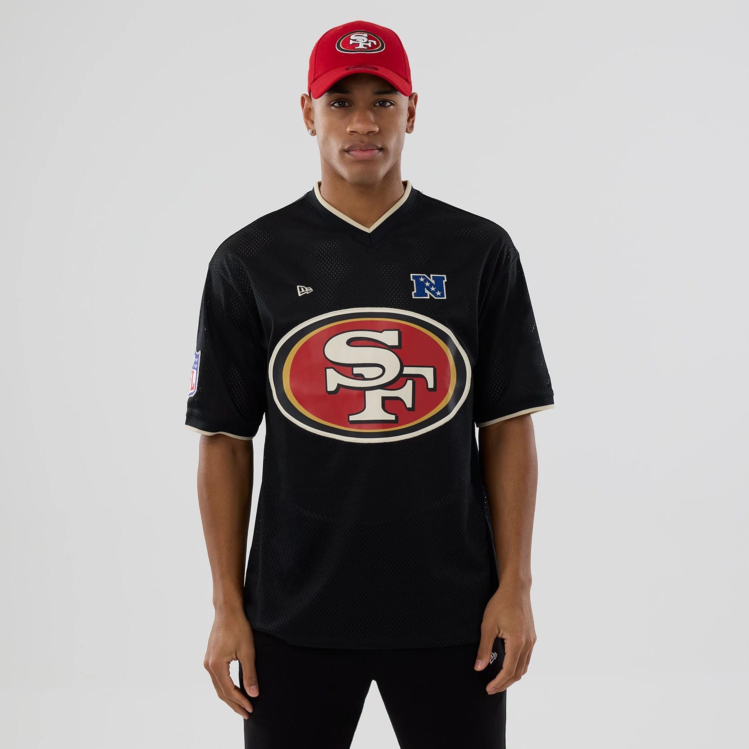 New Era San Francisco 49ers NFL Mesh Black Oversized T-Shirt, front view featuring a large red and gold 49ers logo centred on the chest, an embroidered New Era logo on the upper left chest, styled on a model with a red cap.