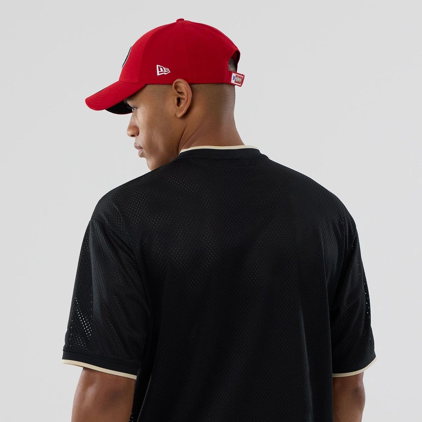 New Era San Francisco 49ers NFL Mesh Black Oversized T-Shirt, back view on a model with a red cap, showing the simple black mesh fabric with contrasting trim on the sleeves and neckline.