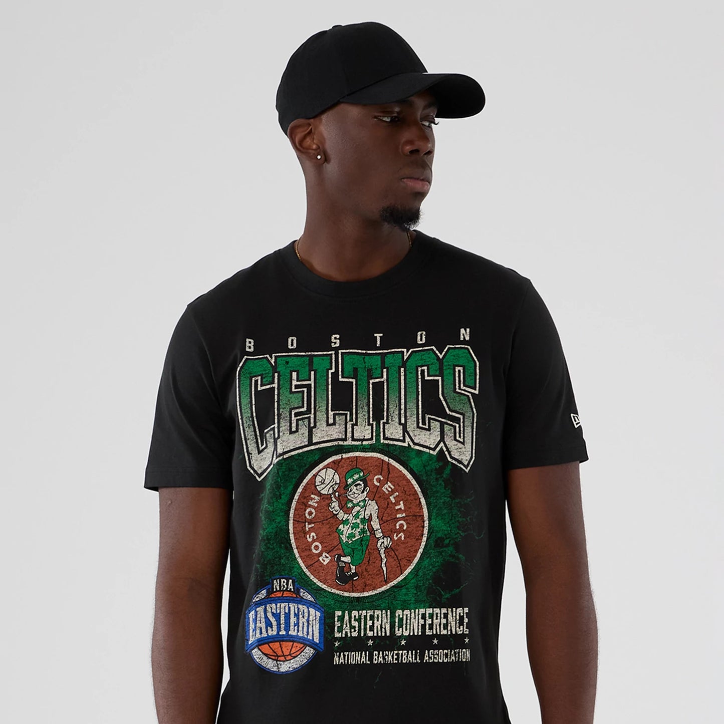 New Era Boston Celtics NBA Hardwood Classic Black T-Shirt, front view on-model showing the large Celtics graphic with lettering and a vintage basketball logo across the chest, paired with a plain black cap.
