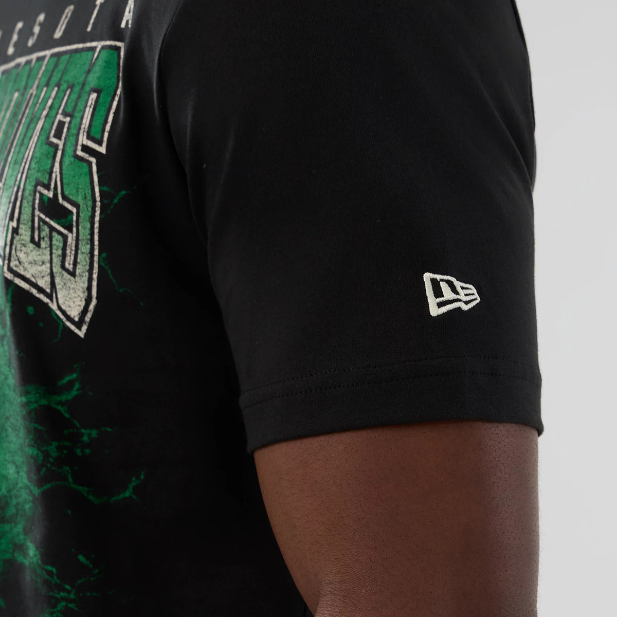 New Era Minnesota Timberwolves NBA Hardwood Classic Black T-Shirt, side view showing the printed Timberwolves graphic in green and white across the chest and an embroidered New Era logo in white on the left sleeve.