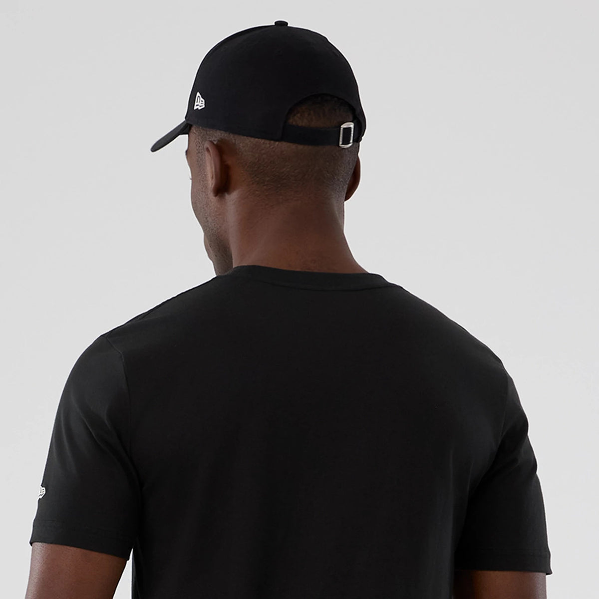 New Era Houston Rockets NBA Hardwood Classic Black T-Shirt, back view on-model showing the plain black rear design with a small printed New Era logo on the left sleeve, paired with a matching black cap with an embossed logo on the side.