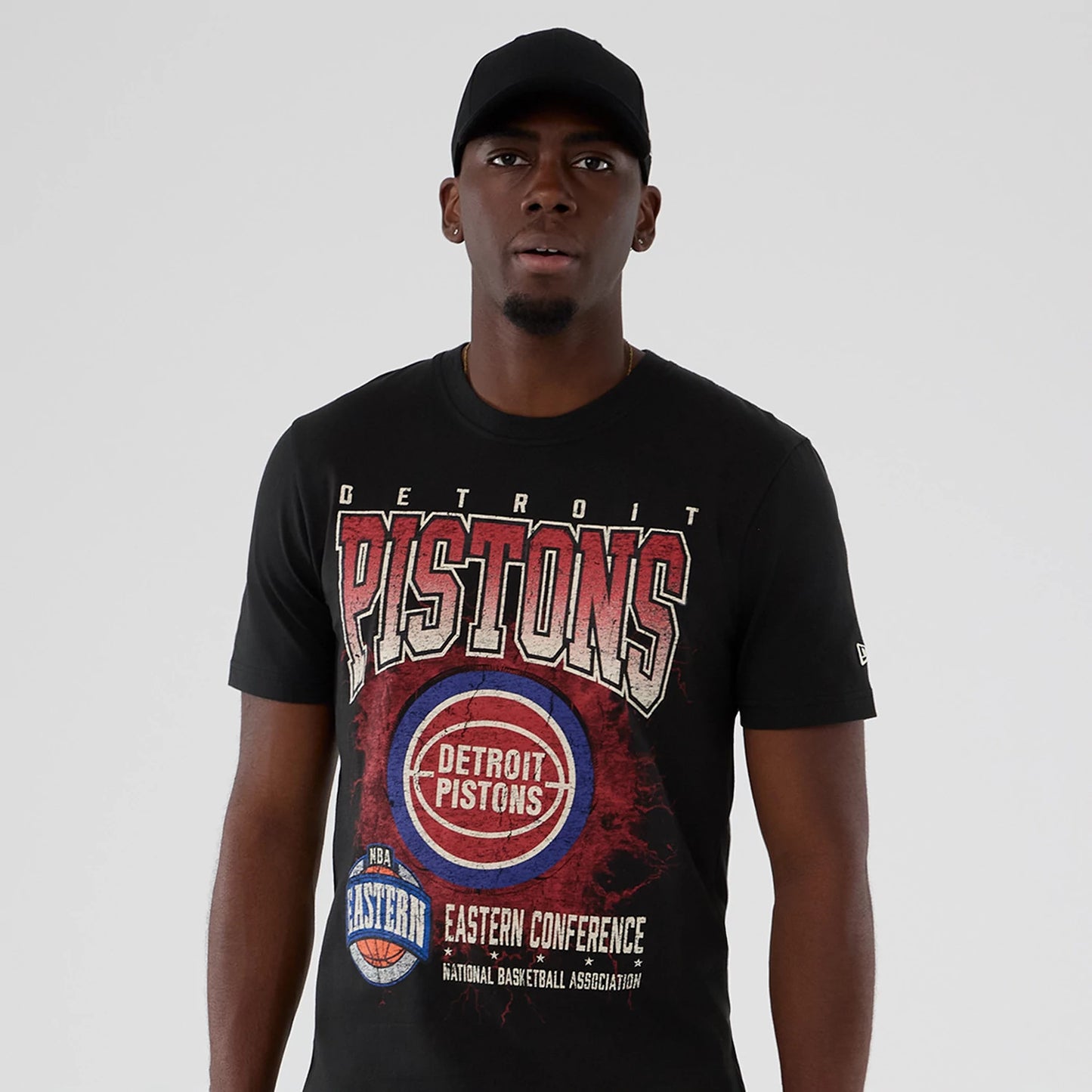 New Era Detroit Pistons NBA Hardwood Classic Black T-Shirt, front view on-model showing large distressed Pistons graphic with basketball and Eastern Conference lettering, featuring an embroidered New Era logo on the sleeve.