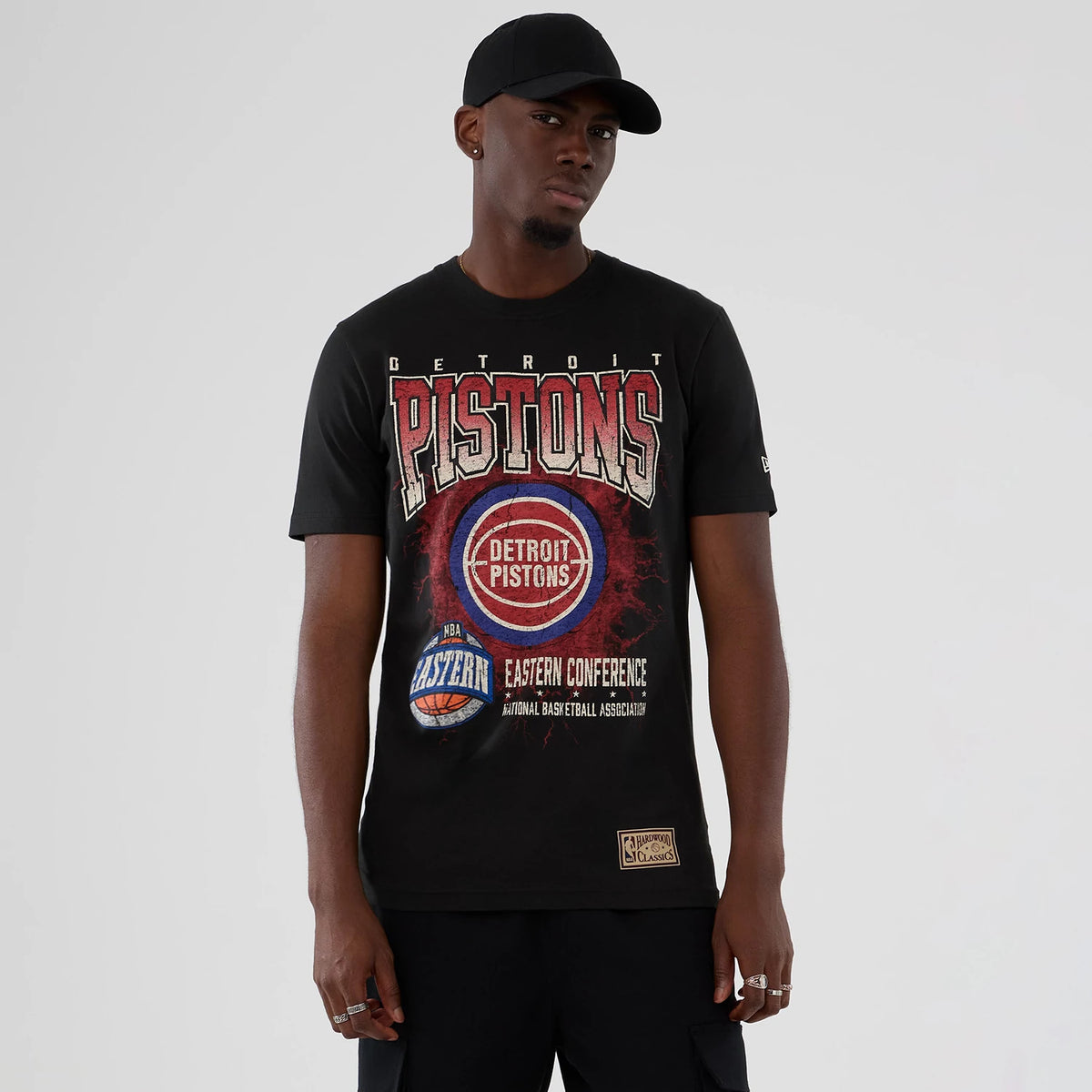 New Era Detroit Pistons NBA Hardwood Classic Black T-Shirt, front view on-model displaying large Pistons lettering across the chest, a central graphic with Eastern Conference text below and a small patch logo near the hem.