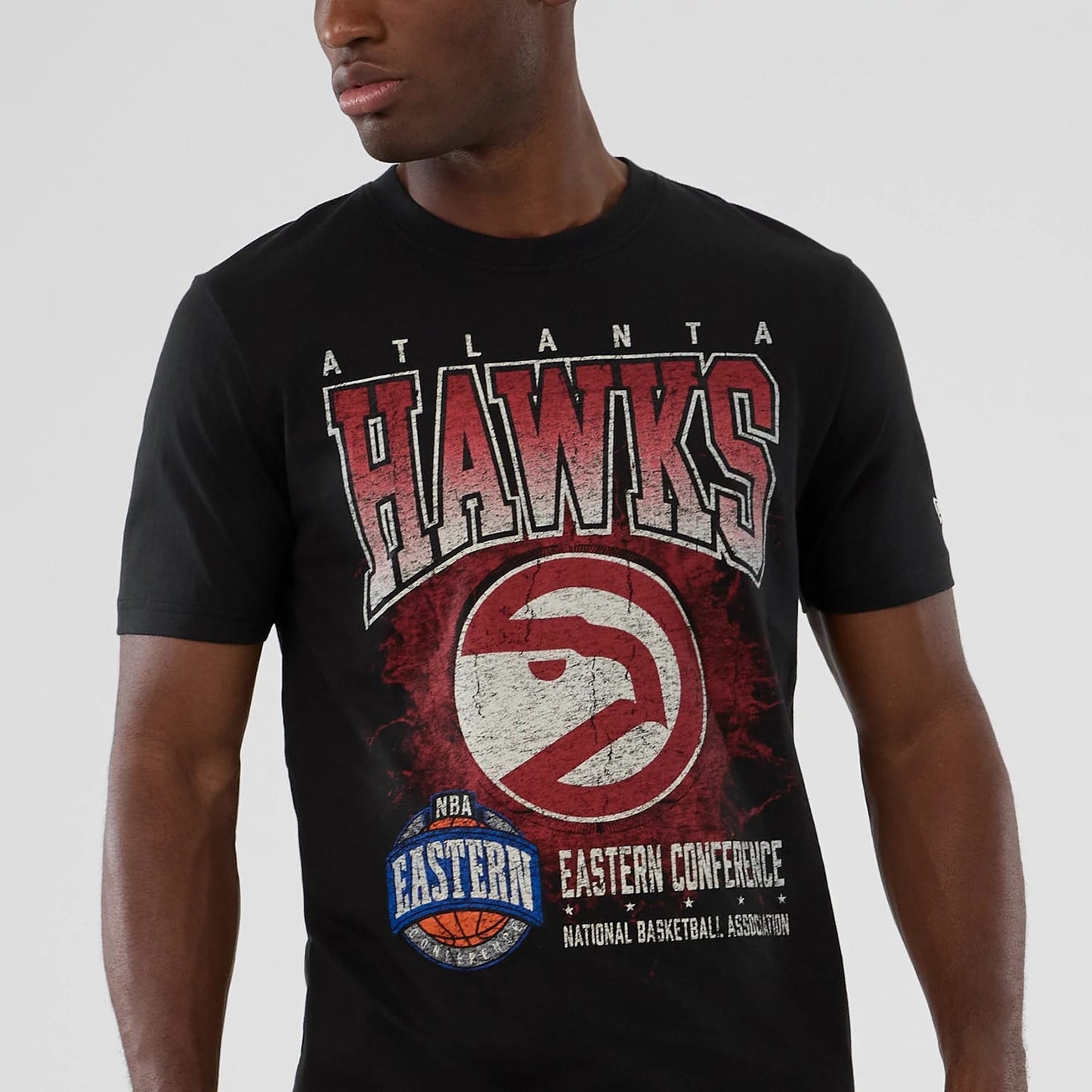 New Era Atlanta Hawks NBA Hardwood Classic Black T-Shirt, front view on a model showing large distressed red and white HAWKS lettering with the team logo below, framed by Eastern Conference and NBA graphics across the chest.