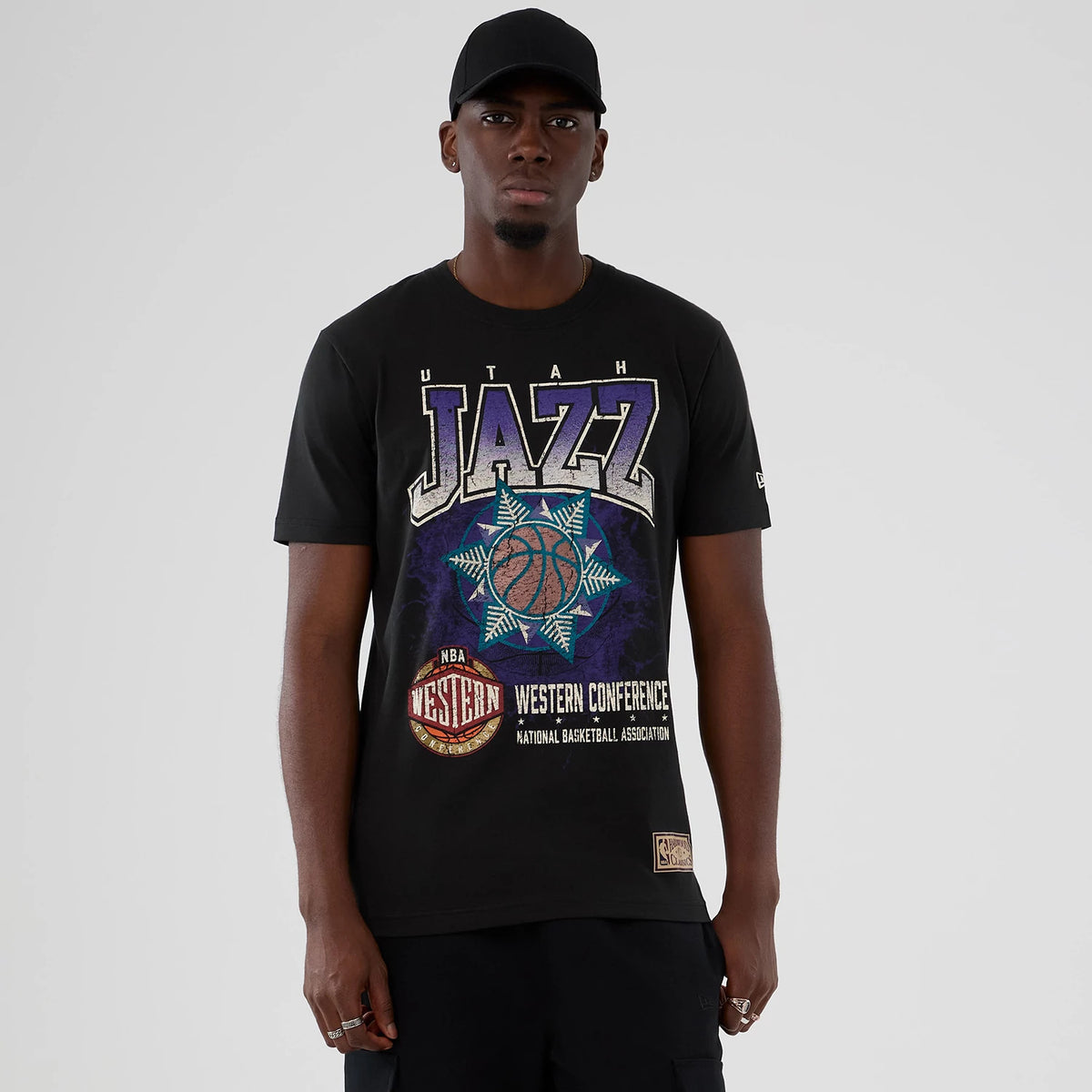 New Era Utah Jazz NBA Hardwood Classic Black T-Shirt, front view on model showing Utah Jazz lettering across the chest with a central basketball graphic, additional Western Conference text, and embroidered New Era logo on the sleeve.